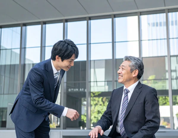 Coworkers greeting each other with 'Otsukaresama desu' in an office